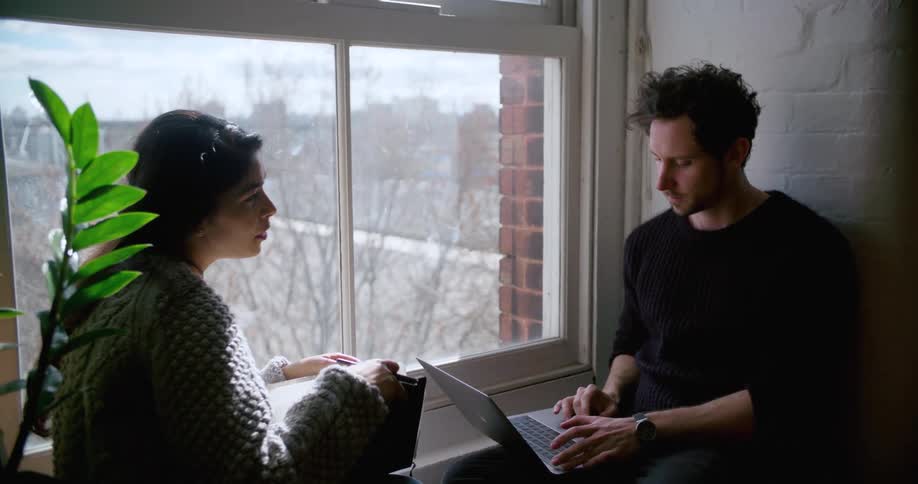 Two people are sitting next to a window and are working on a project together