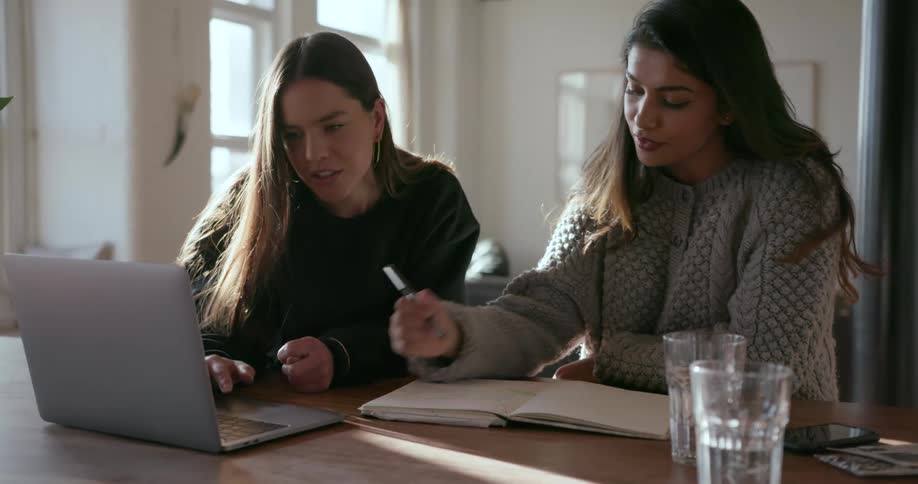 Two girls talk while looking at a laptop