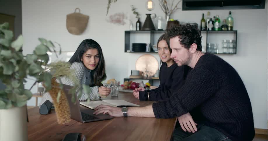 Two women and a man sit down and look at laptop together and talk