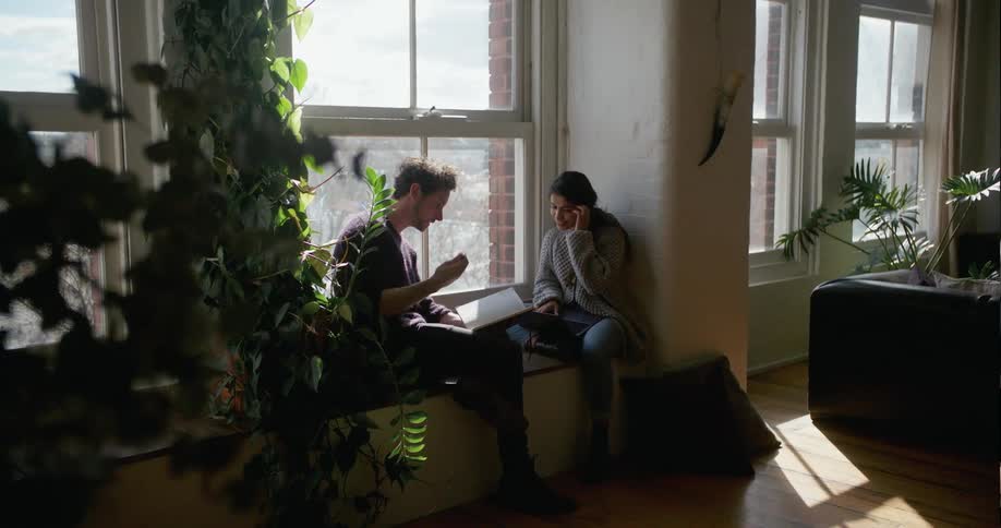Two people talk and go through a book by the window