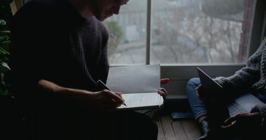 A man takes notes while talking with another person