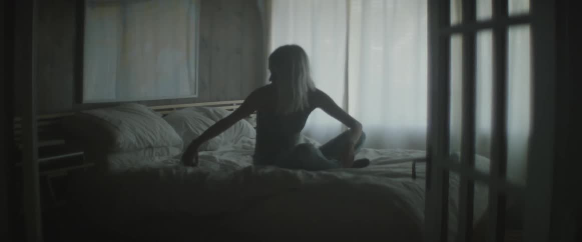 A woman wakes up in bed and checks her phone before getting up