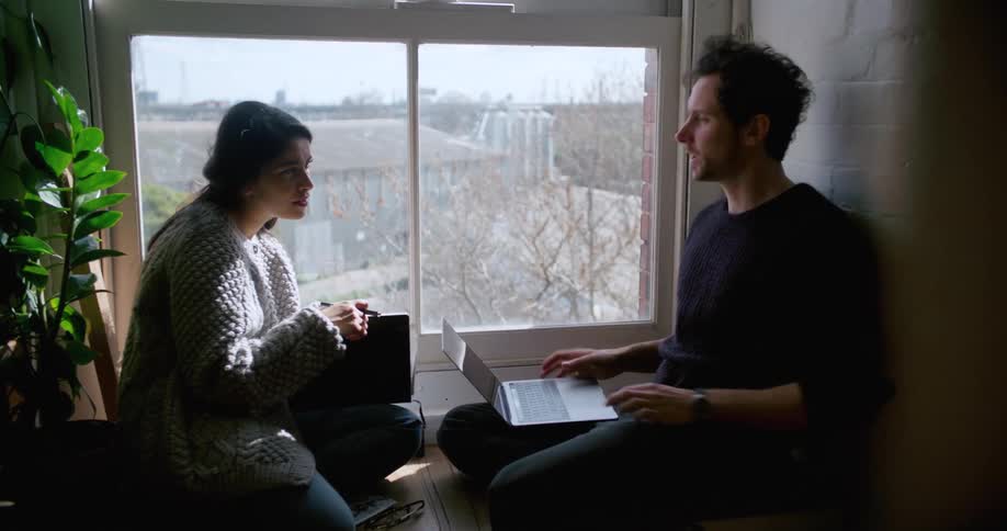 A man and woman have a conversation sitting by a window