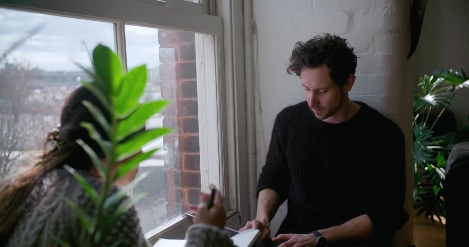 A man and woman work while sitting next to a window
