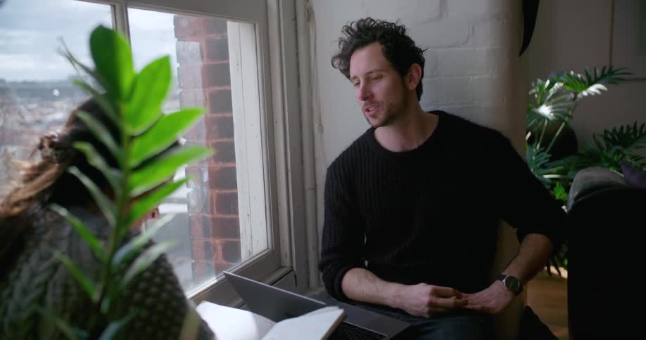 A man and woman have a conversation sitting by a window