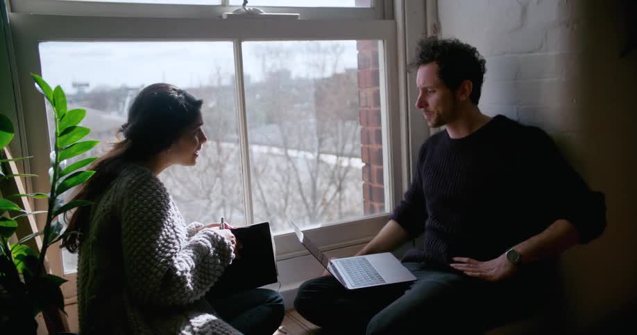 A man and woman talk while sitting next to a window