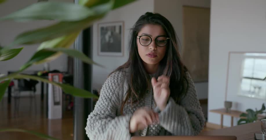 A woman puts on glasses and looks at something on the laptop