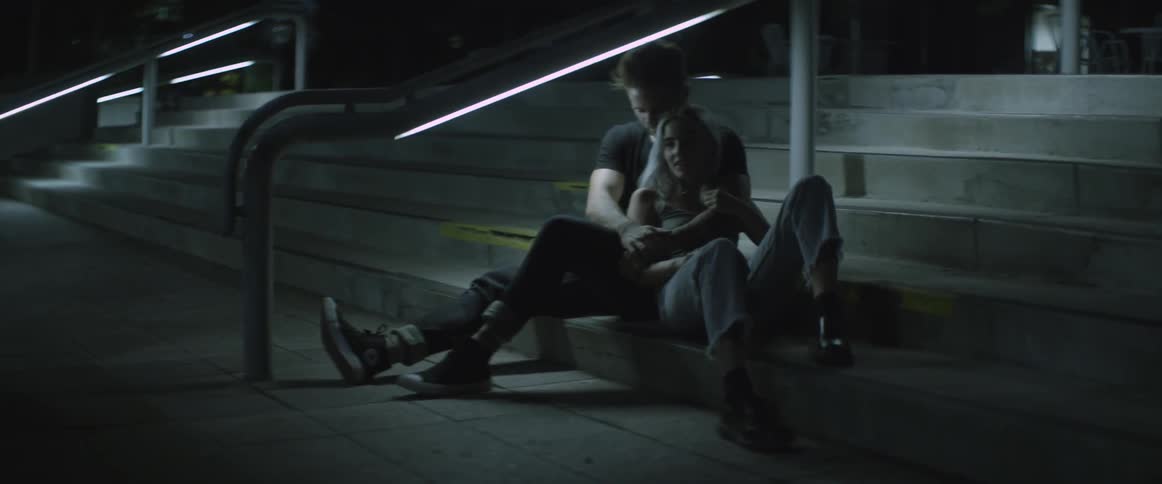 Couple sitting closely  on stairs outside a closed building at night