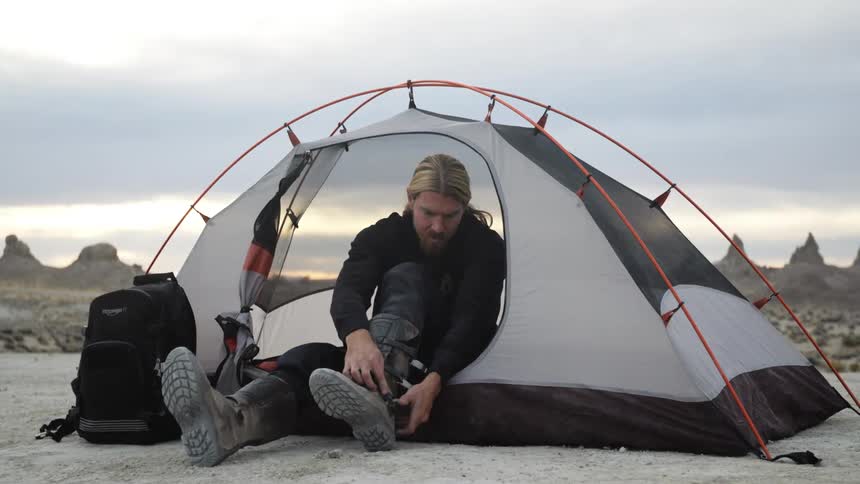 Blonde man sitting inside a tent in the desert at evening takes off his boots