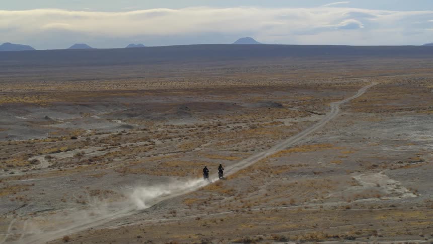 Two people are riding motorcycles through the desert