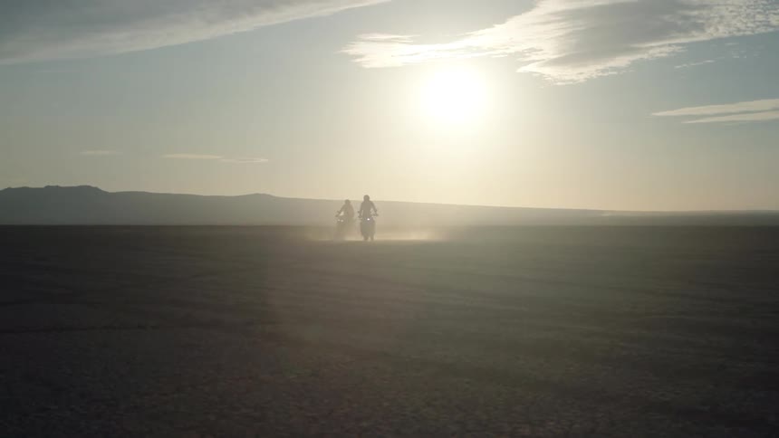 Two people ride their dirt bikes in the desert at sunrise