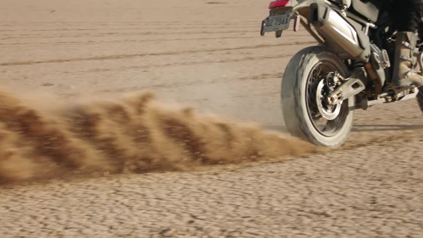 Female biker with boots black pants backpack and motorcycle helmet skids on desert