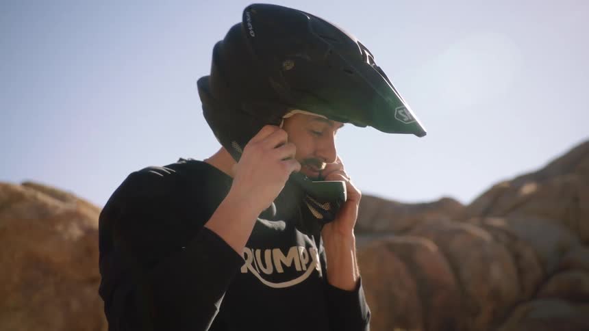 A man sitting atop a motorcycle puts on his helmet and fastens the chin strap
