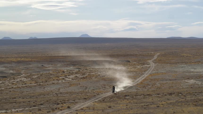 Two motorcycles stir up dirt as they travel on a dirt path in the desert
