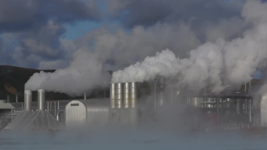 Fog flows past factory releasing smoke into air near a mountain