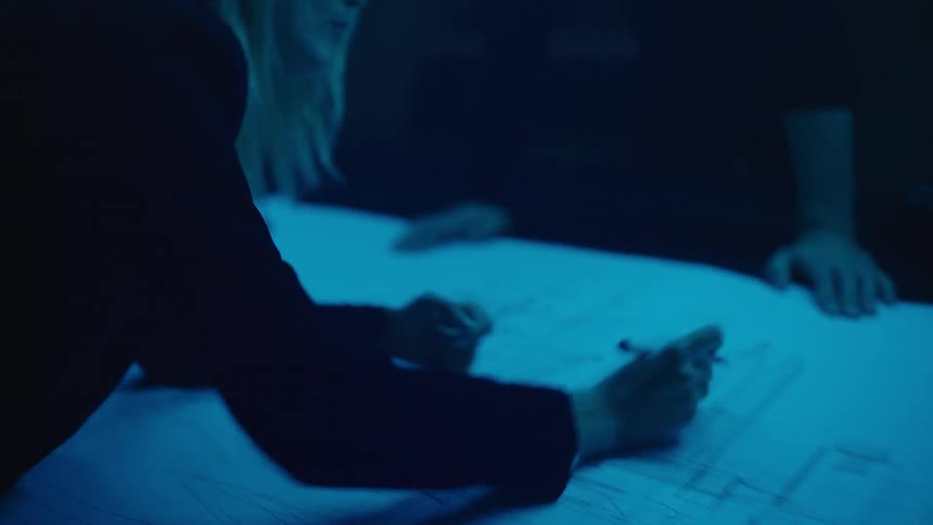 A man and woman talk as she makes changes to a blueprint