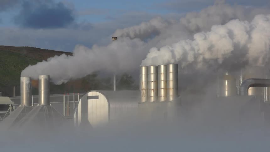 Smoke rises from chimneys of factory near sitting near base of mountain on cloudy day