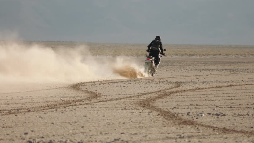 Biker with black motorcycle helmet jacket pants and backpack rides motorcycle in the desert