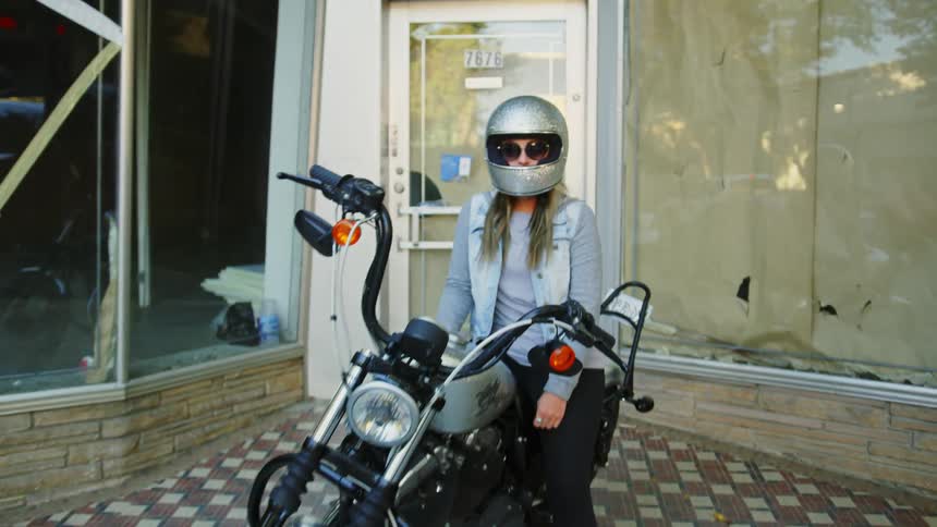 Woman sits on motorcycle in front of empty storefront