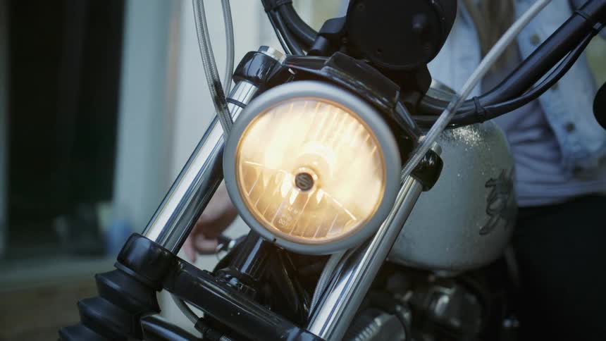 Woman with denim jacket black and black pants switches on motorcycle headlight in the street