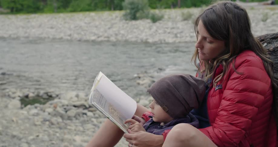 A woman and child read a book by the stream