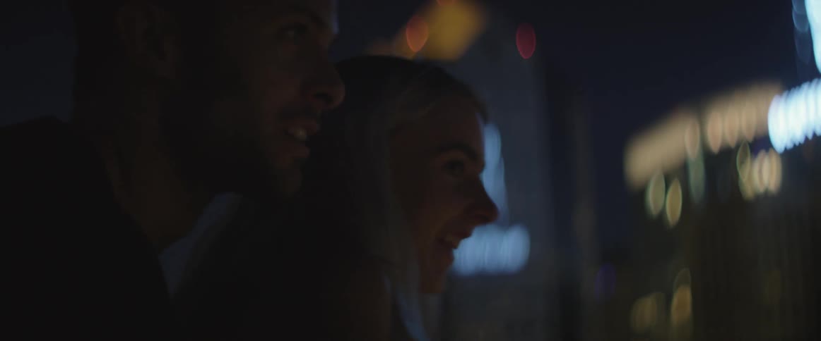 A man and woman stand in a well lit city at night