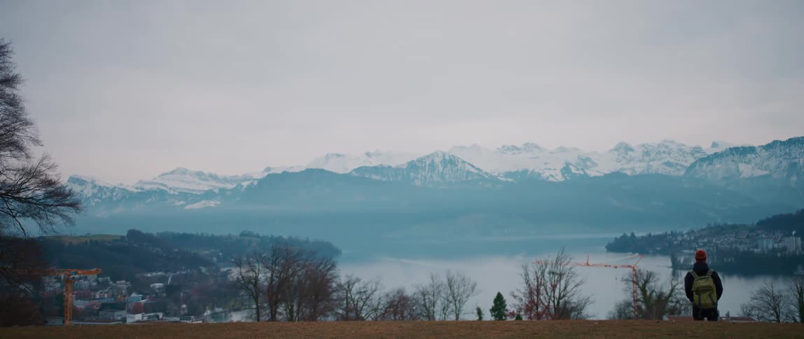 A man stands and looks out over the water and towards the mountains