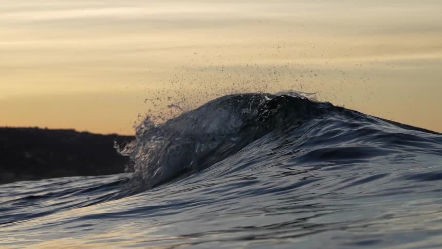 Ocean waves roll and splash into shore near the hills