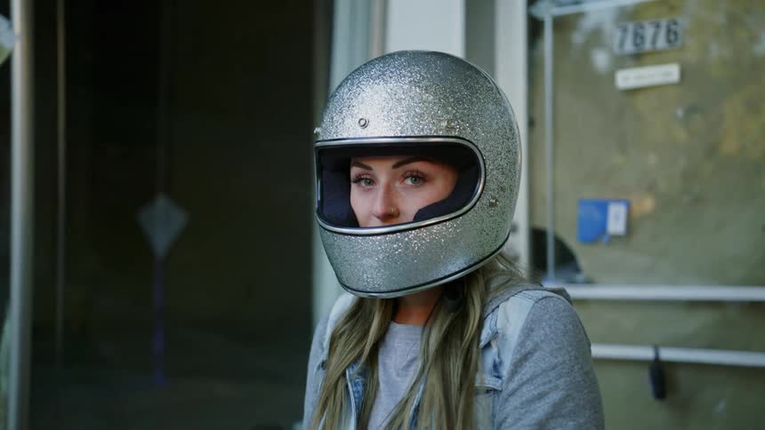 A woman wearing a silver glitter motorcycle helmet is in front of a door