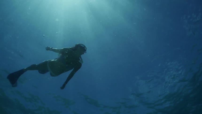 Woman in bikini googles and a pair of flippers swims underwater