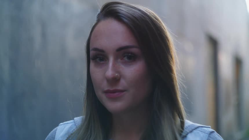 A woman smiles while standing in an alley near a building