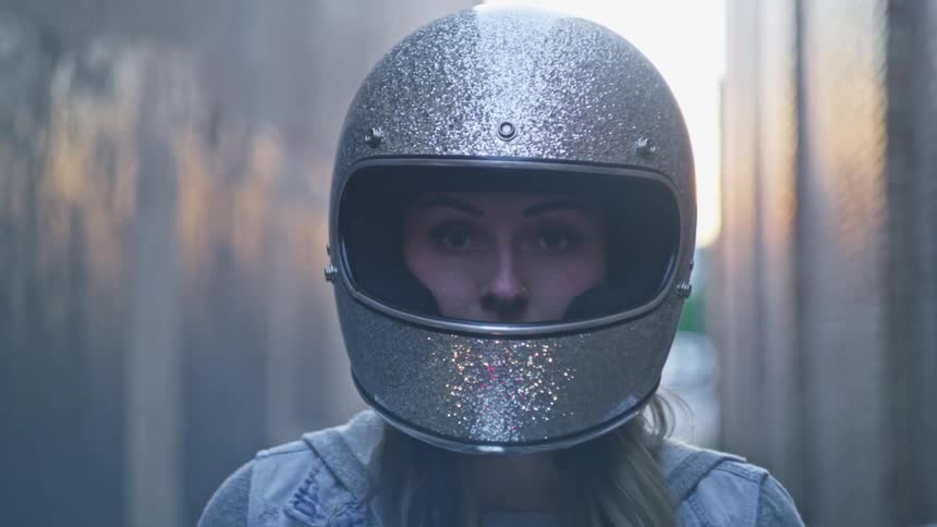 Female biker with silver motorcycle helmet and denim jacket looks at camera