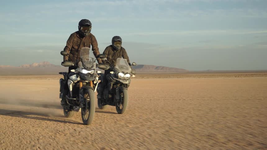 Two men stand as they ride motorcycles through the desert