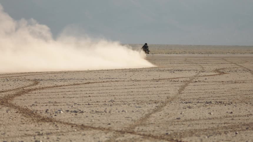 Male biker with motorcycle helmet black jacket and pants skidding across the desert sand