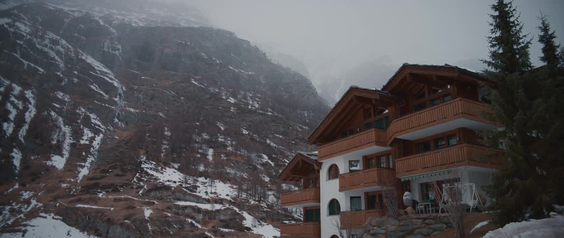Snow falling over a big house at the bottom of a tall mountain at winter