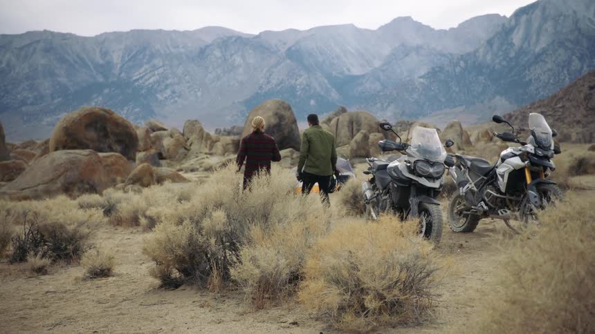 Two young men walk away from parked motorcycles into a tent in the wilderness near the mountains