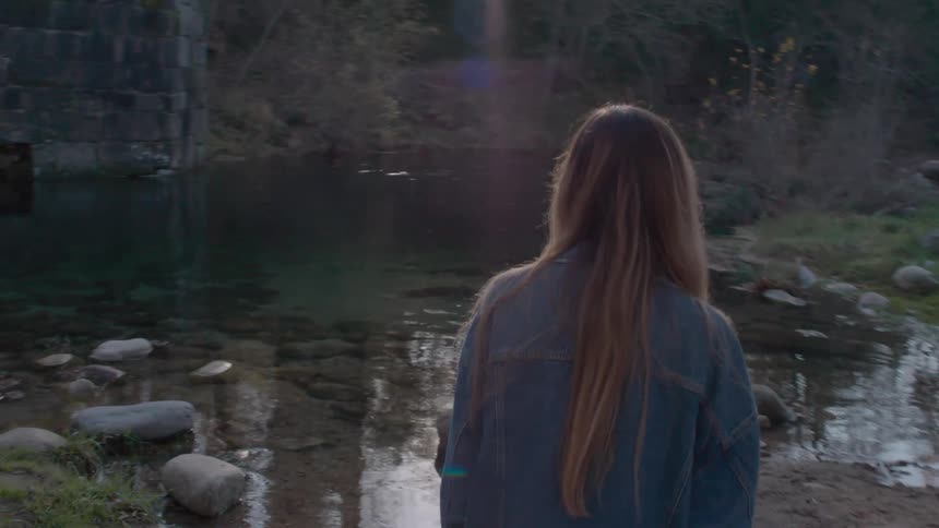 A woman slowly approaches a stream in the wilderness during the day