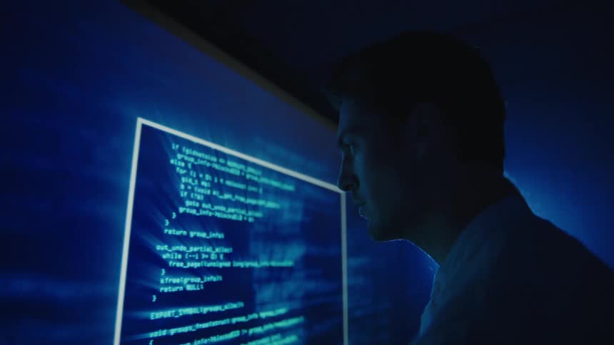 Two people read fast moving code and text on a large screen
