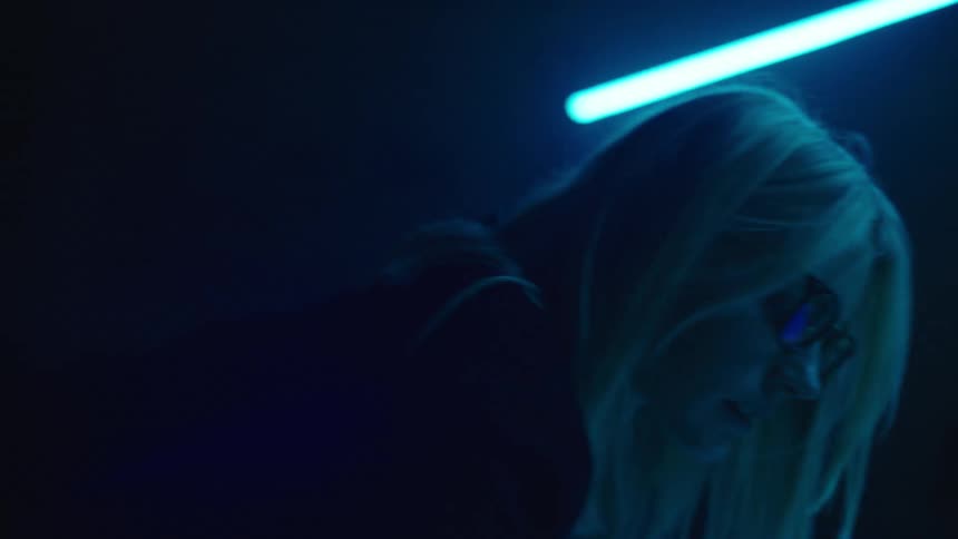 Young blonde woman wearing glasses draws with a pen on a blueprint over a table inside a dimly lit office
