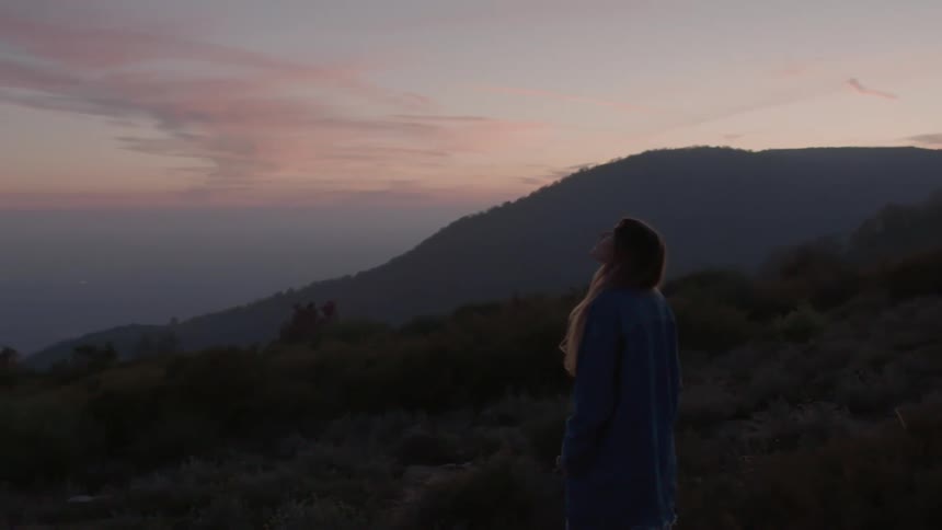 A woman gazes at the sky while standing high in the hills at sunrise