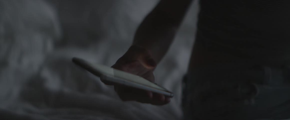 Blonde woman picking up and using a smartphone that was lying on her bed