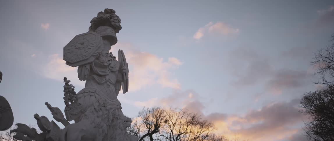 Statue stands outdoors near leafless trees under bright and dark clouds