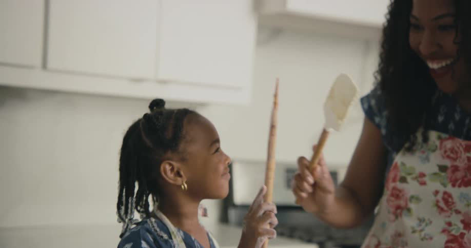 A mother and daughter high five with spatulas while cooking