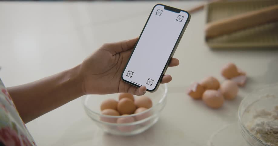 A woman looks at her smartphone while standing before a table covered in cooking ingredients