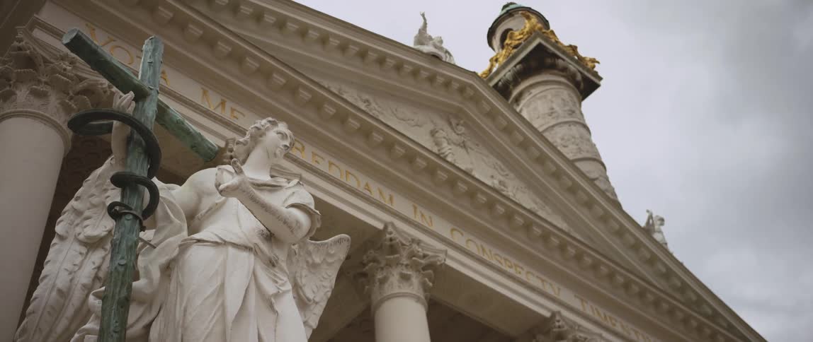 A statue outside of a building with a sculpted facade on a cloudy day