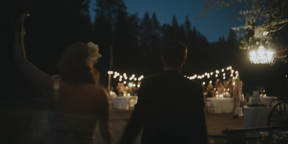 A man and woman holding hands walk toward a wedding party