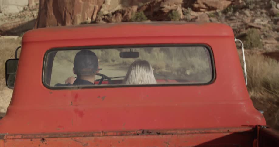 Two people are traveling in a red truck by a canyon