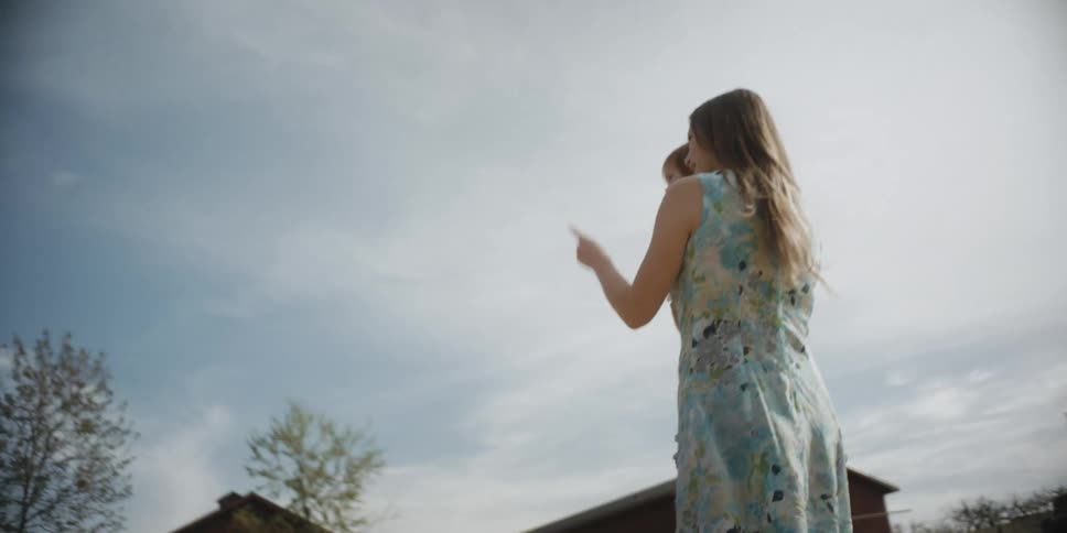 A woman is carrying her child and pointing things out on a farm