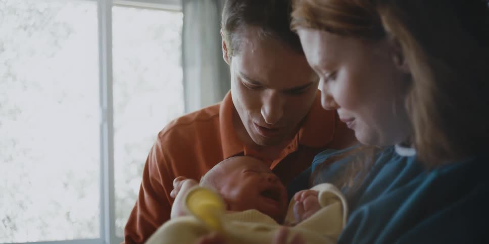 A man and woman holding a baby next to a window