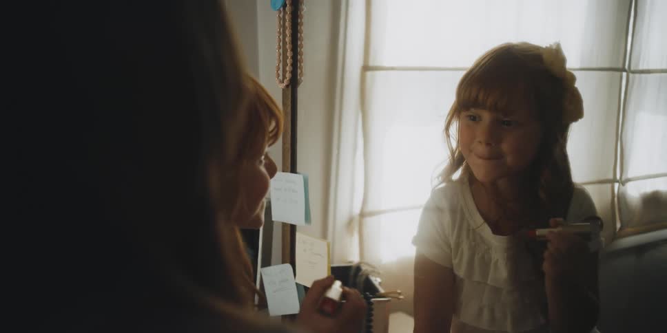 A girl puts on makeup as a woman watches
